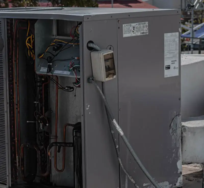 Close-up of an outdoor air conditioning condenser unit with its service panel open, showing copper refrigerant lines and wiring