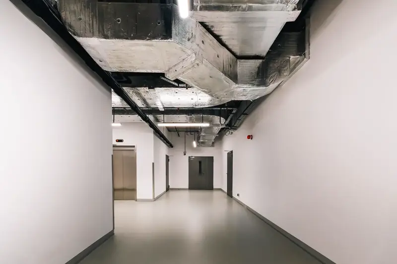 Exposed metal HVAC ductwork running along the ceiling of a bright hallway