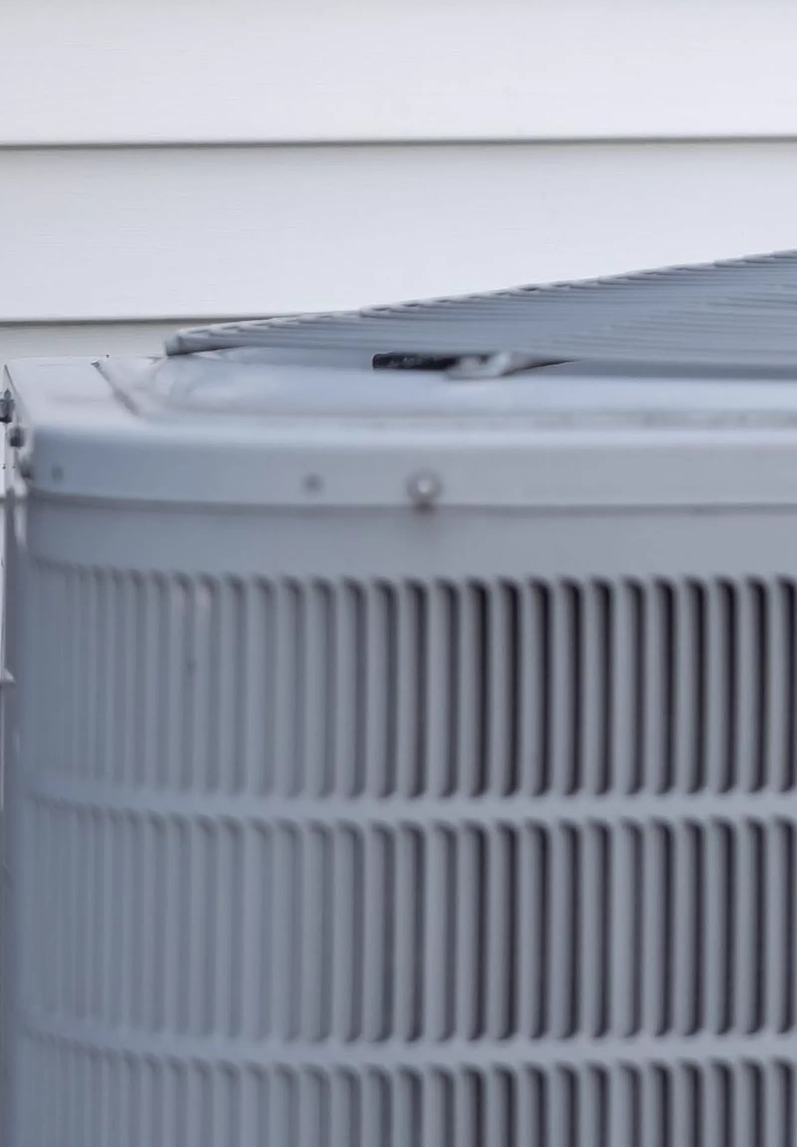 Close-up of a ground-level outdoor HVAC unit with louvered panels beside a home's exterior siding