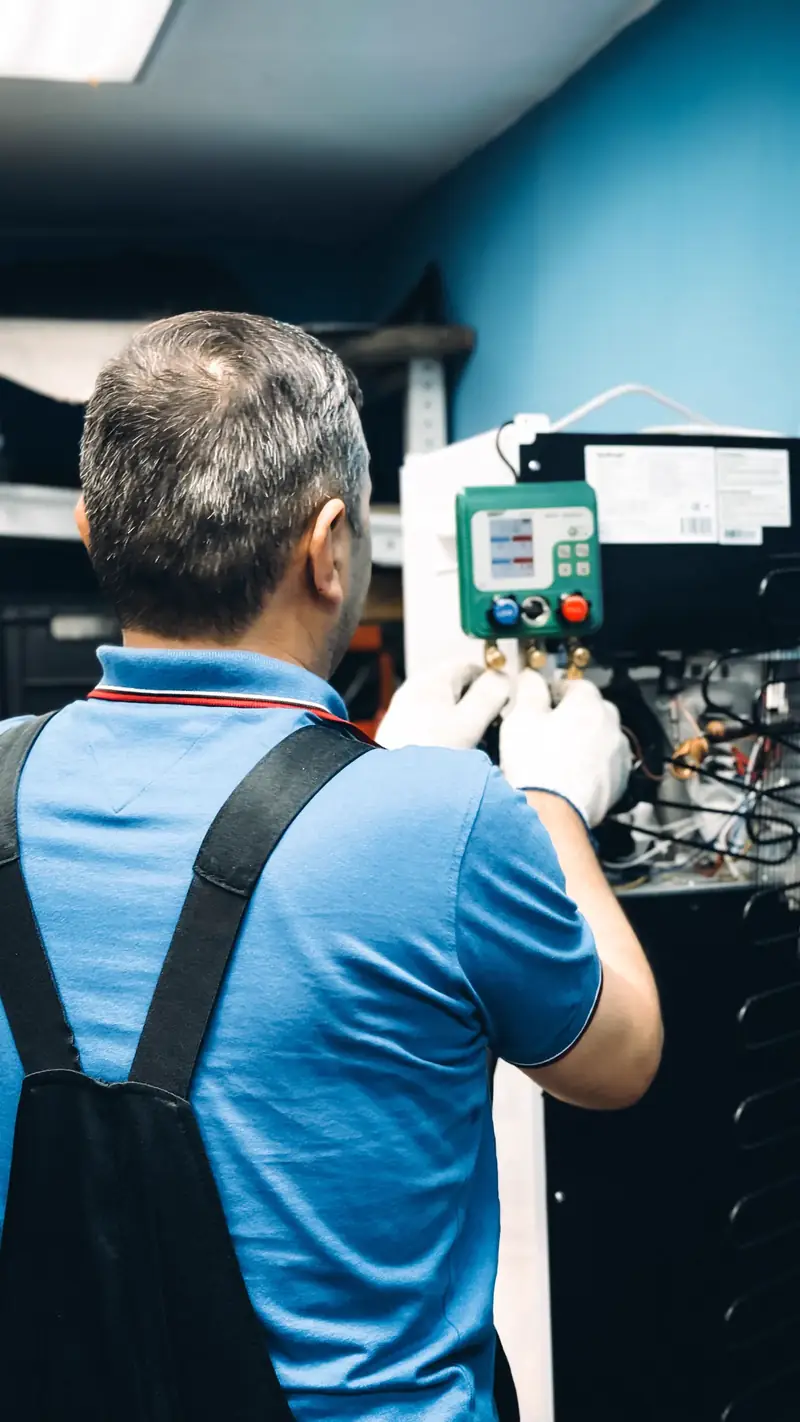 HVAC technician servicing an indoor unit with exposed coils using a digital manifold gauge