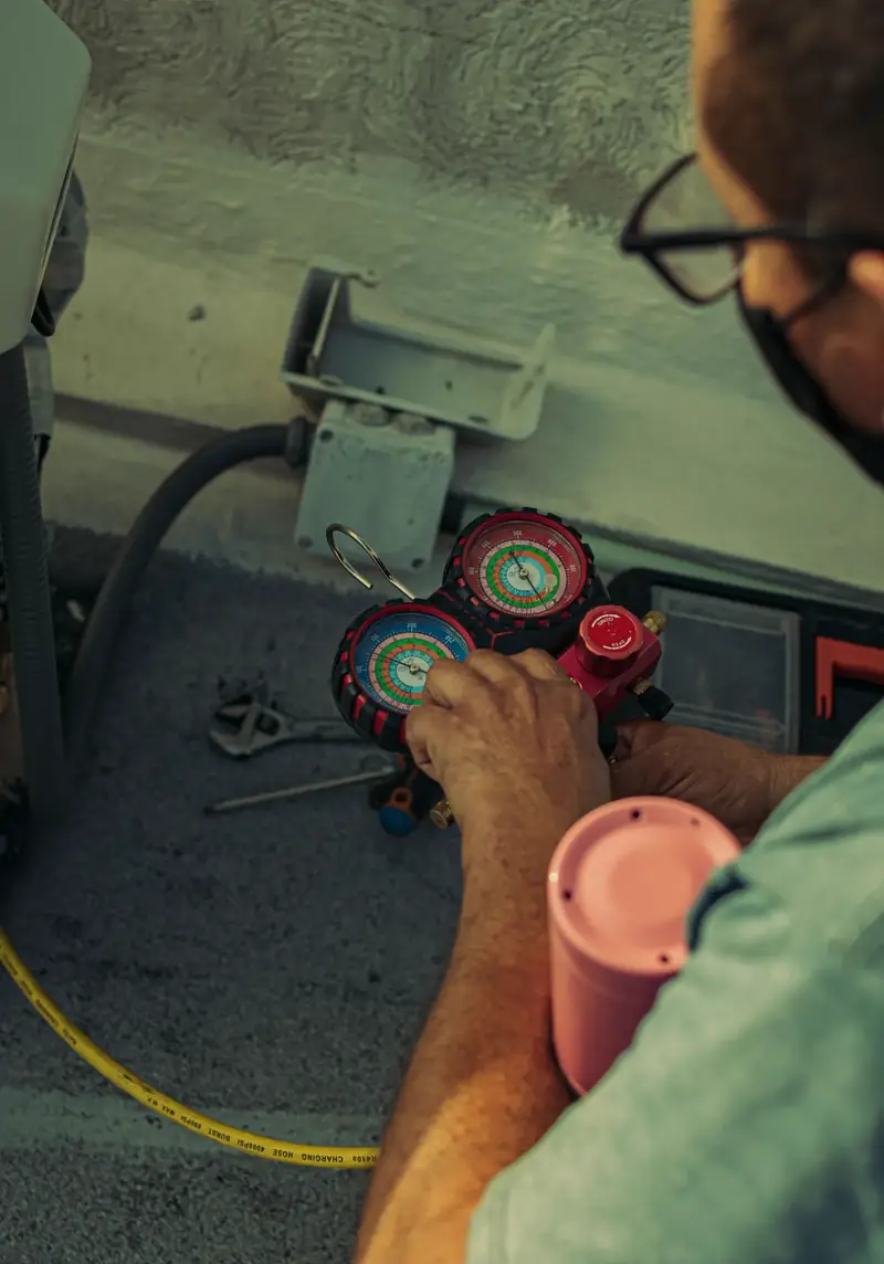 HVAC technician's hands holding red and blue refrigerant manifold gauges during air conditioning maintenance