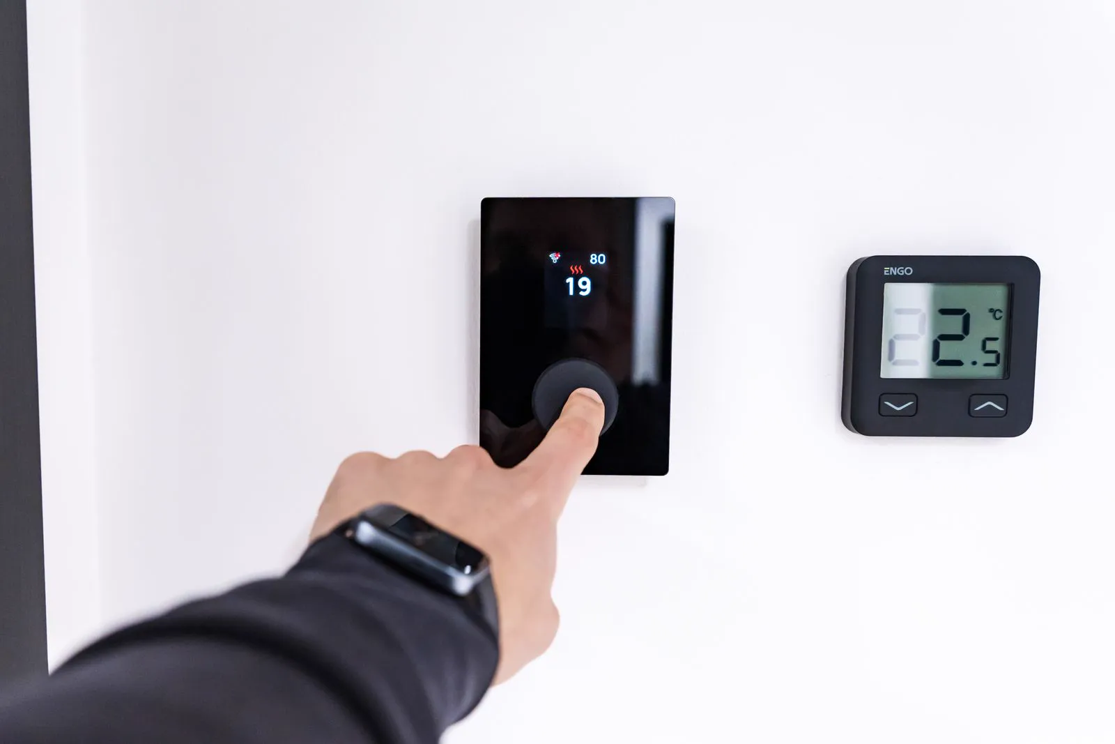 Finger pressing a modern digital wall thermostat displaying the temperature setting