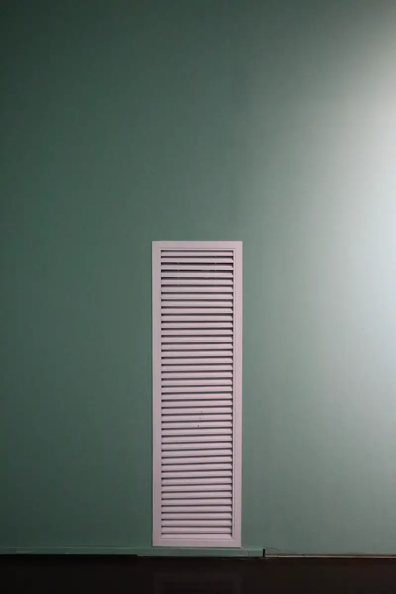 White louvered air vent grille on a mint green interior wall
